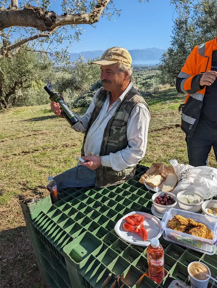 Mann mit einer Flasche Liberis Olivenöl bei einer Essenspause im Olivenhain