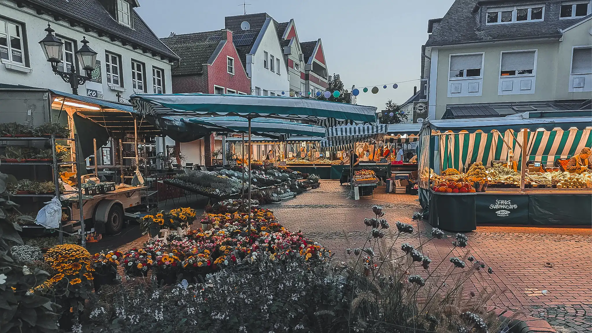 Wochenmarkt mit Blumen, Gemüse und beleuchteten Marktständen